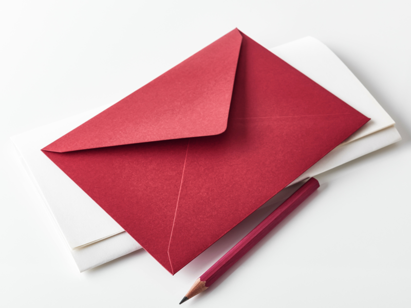 ein roter Briefumschlag und Briefpapier liegt auf einer weißen Fläche, daneben liegt ein roter Stift