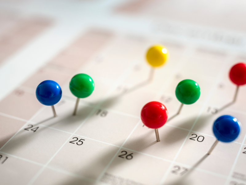 Papierkalender mit Kacheln in denen Zahlen geschrieben sind, darauf sind bunte Pinnadeln in einige Kacheln gepinnt