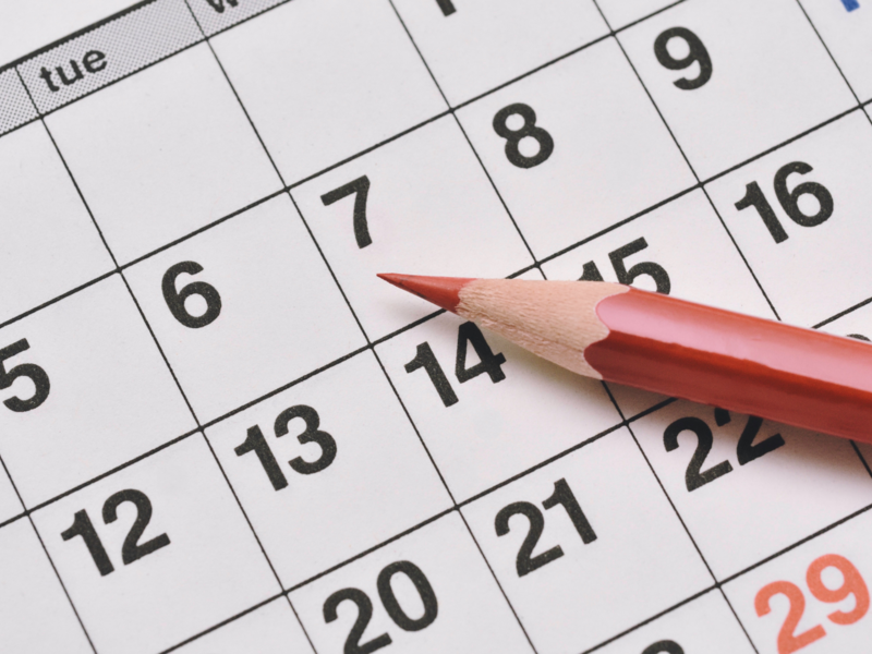 Papierkalender mit Kacheln in denen Zahlen geschrieben sind, darauf liegt ein roter Stift